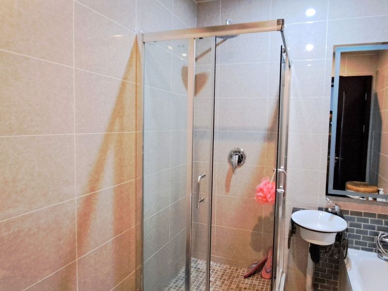 A modern bathroom featuring a glass shower enclosure, wall-mounted basin, and contemporary tiled walls with a sleek integrated mirror.