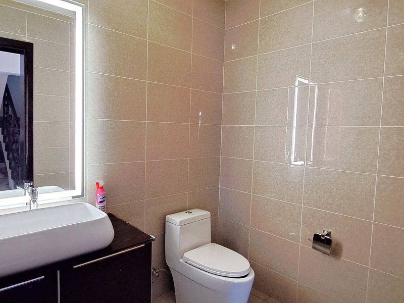 A modern bathroom featuring a vessel sink on a dark vanity cabinet, a backlit mirror, and neutral wall tiling.