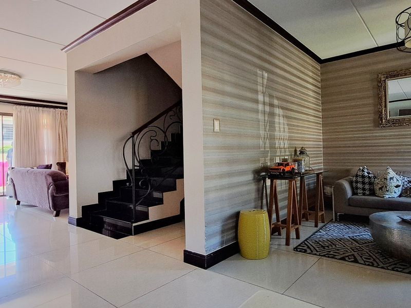 Spacious open-plan living area featuring tiled flooring, a central staircase with decorative wrought iron balustrade, and sliding glass doors leading to an outdoor space.