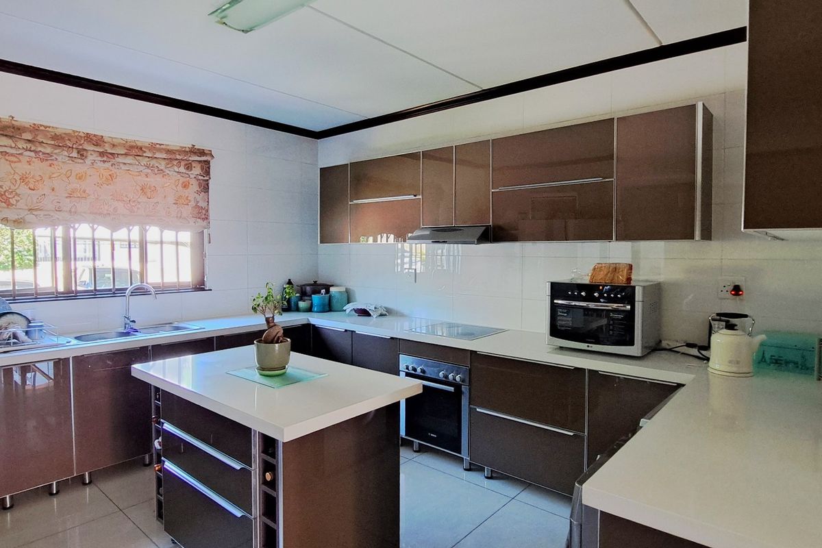 Modern kitchen featuring high-gloss cabinetry, a central island with stone countertops, built-in oven, hob, extractor fan, and tiled finishes throughout.