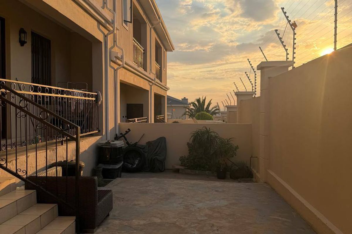 Rear exterior view of a townhouse featuring a paved courtyard, tiled staircase with wrought iron railings, and perimeter wall with electric fencing.