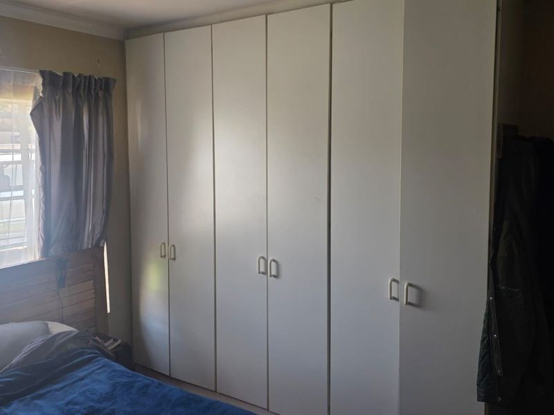 A bedroom featuring a large wall-to-wall built-in cupboard unit with white doors and a window providing natural light.