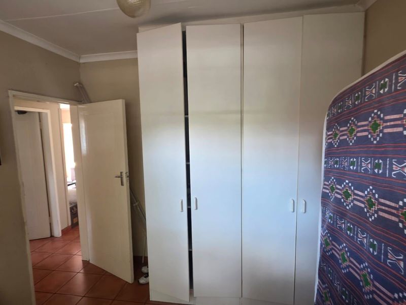 A bedroom featuring built-in white wardrobes and tiled flooring, providing functional storage space within the room.