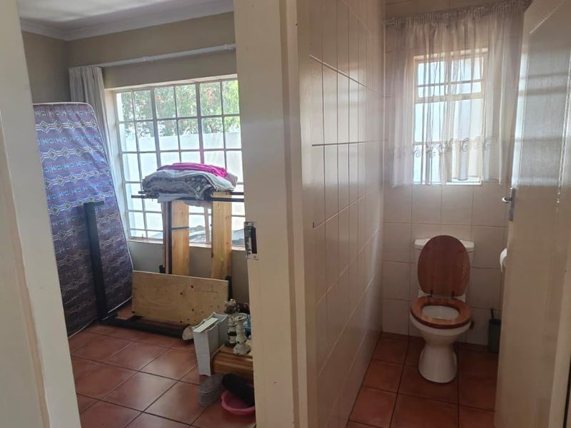 A functional bathroom featuring ceramic floor and wall tiles, equipped with a standard toilet and window, currently showing signs of wear.