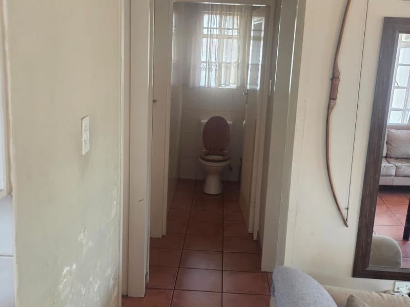 A hallway with tiled flooring leading to a separate toilet, showing visible wall surface damage and peeling paint.