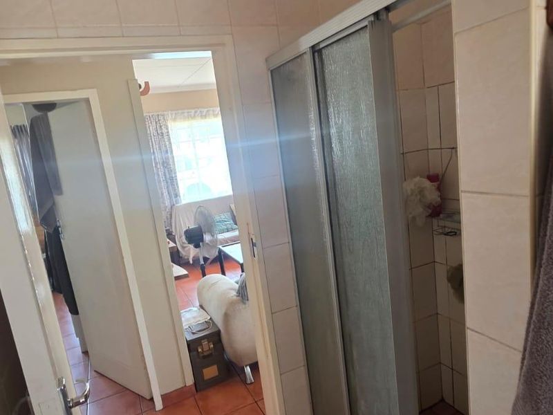 A functional bathroom featuring a shower enclosure with tiled walls and flooring, showing signs of age and wear.