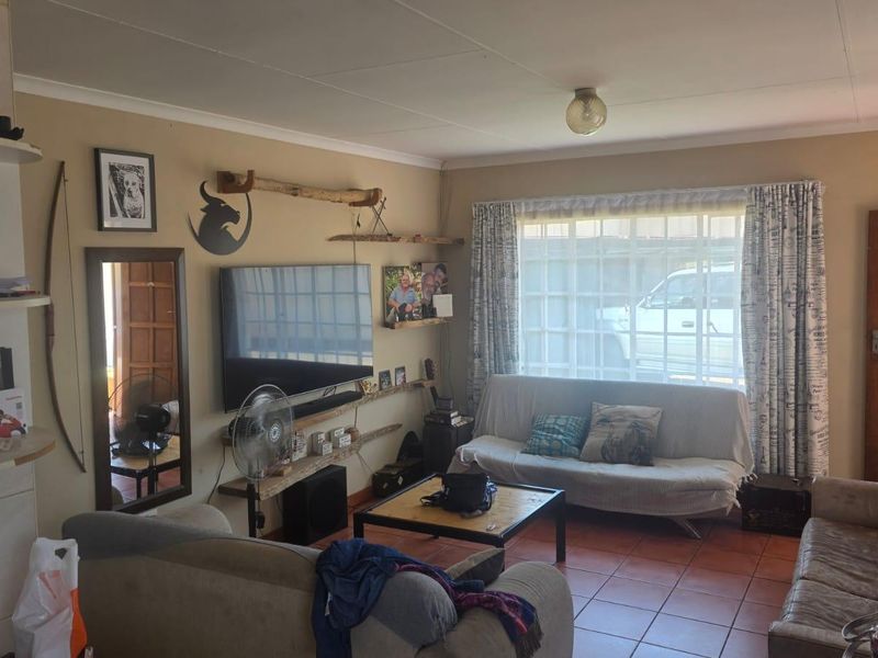 A living room featuring tiled flooring, a coved ceiling, and a window with security bars, providing a functional and lived-in space.