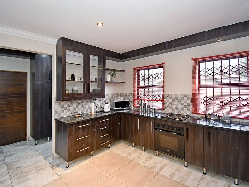 A well-maintained kitchen featuring dark wood cabinetry, granite countertops, built-in oven and hob, and tiled flooring with a neutral backsplash.