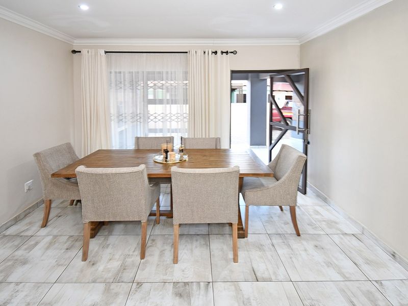 A bright and well-maintained dining room featuring modern wood-look tiled flooring, recessed downlighting, and direct access to the exterior through a sliding door.