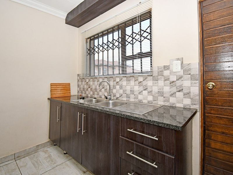 A functional scullery area featuring dark wood cabinetry, granite countertops, a stainless steel sink, and modern tiled backsplash.