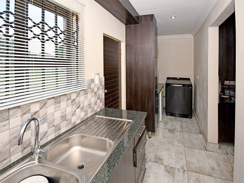 A functional scullery featuring granite countertops, a stainless steel sink, tiled backsplash, and built-in cabinetry with ample storage space.