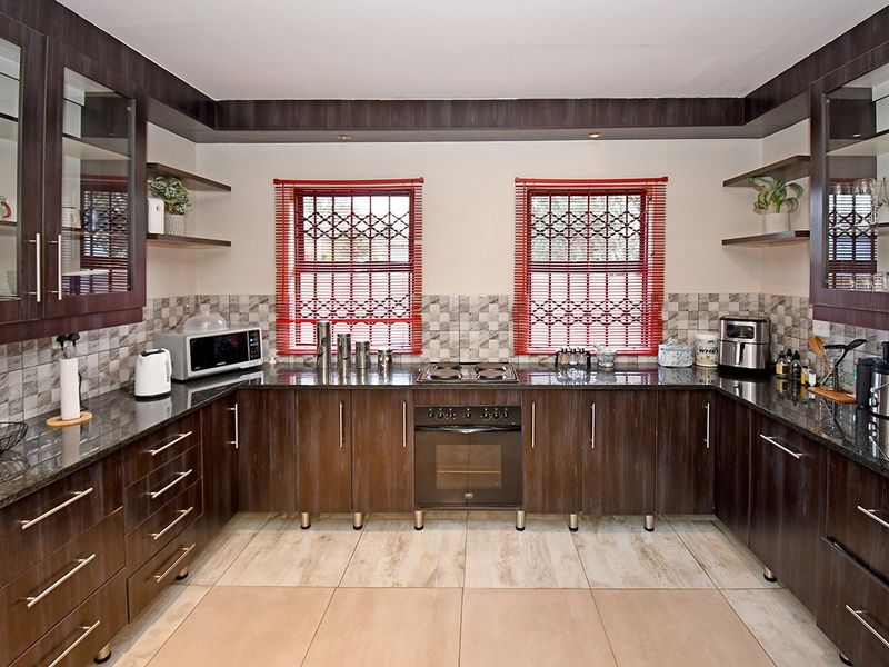 A well-maintained kitchen featuring dark wood cabinetry, granite countertops, a tiled backsplash, and built-in cooking appliances with security gates on the windows.