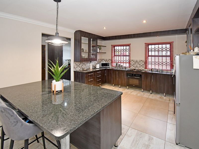 Modern kitchen featuring dark wood cabinetry, granite countertops, a central island, built-in oven, and tiled flooring with ample natural light.