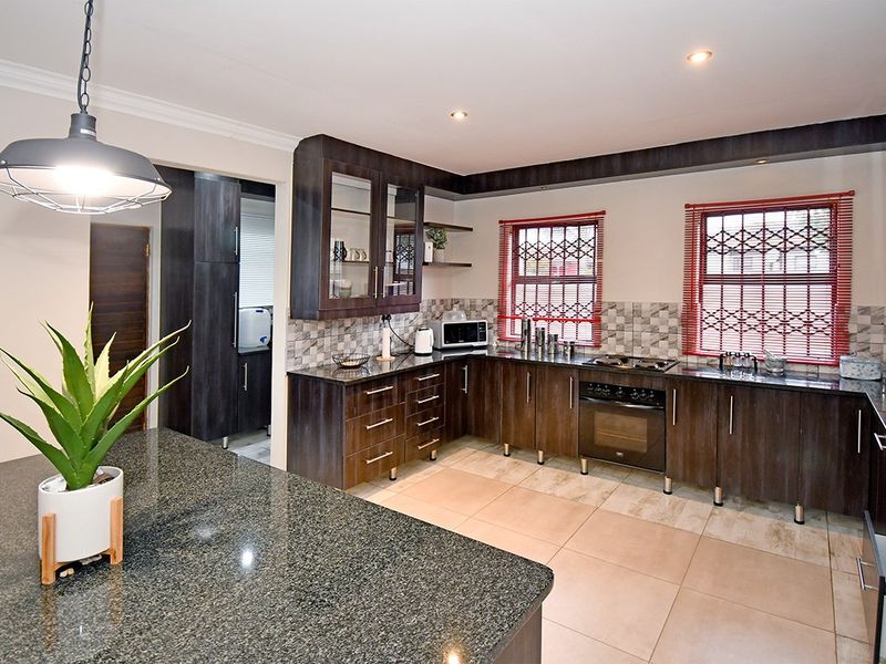 Modern kitchen featuring dark wood cabinetry, granite countertops, built-in oven with gas hob, tiled backsplash, and a central island with pendant lighting.