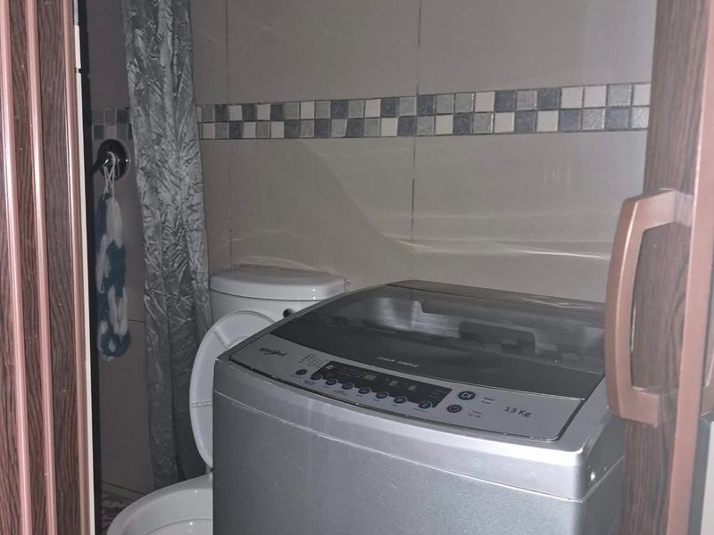A compact laundry area featuring tiled walls and a toilet, currently accommodating a washing machine.