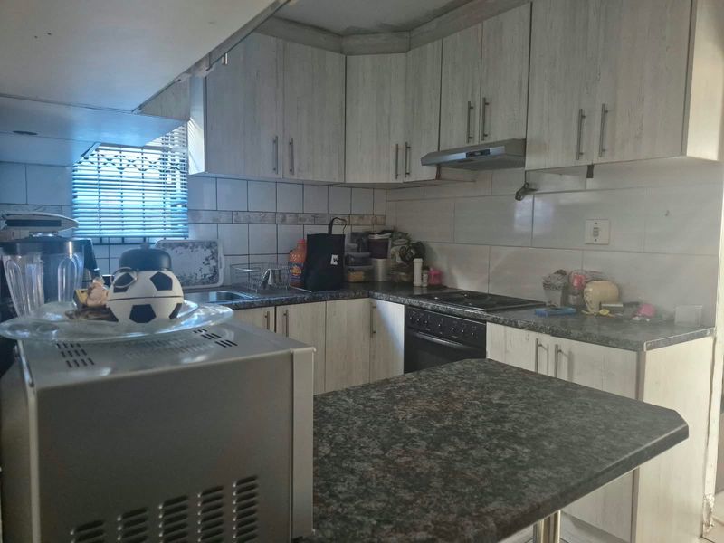 Functional kitchen featuring light-toned cabinetry, dark laminate countertops, tiled backsplash, and integrated cooking appliances.