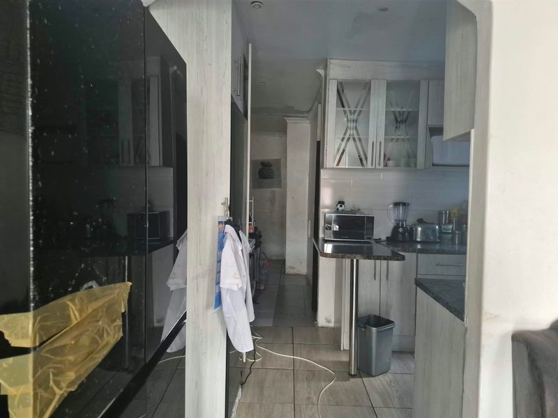 A compact kitchen featuring light-toned cabinetry, tiled flooring, and a breakfast bar, currently showing signs of wear and requiring cosmetic updates.