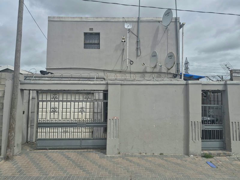 Front elevation of the property featuring a paved driveway, secure perimeter wall with razor wire, and gated access points.