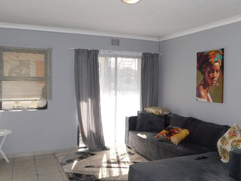 A well-lit living room featuring neutral grey walls, tiled flooring, and a sliding glass door that provides access to the exterior.