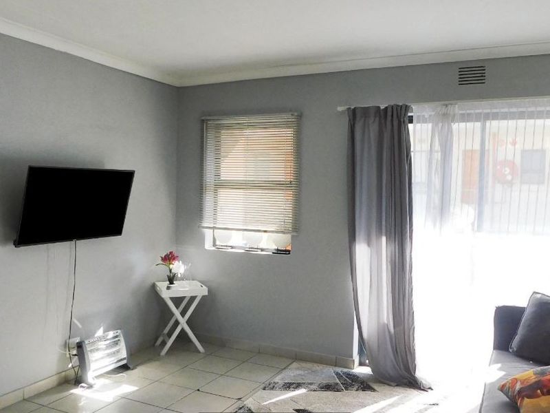 A living room featuring tiled flooring, a sliding glass door with curtains, and a window with venetian blinds.