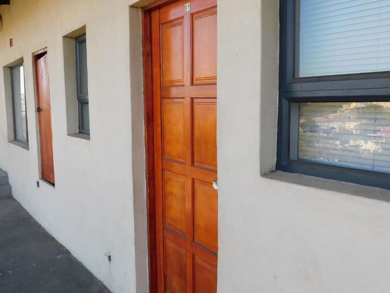 Exterior view of an apartment entrance featuring a timber door and aluminium window frames along a concrete walkway.