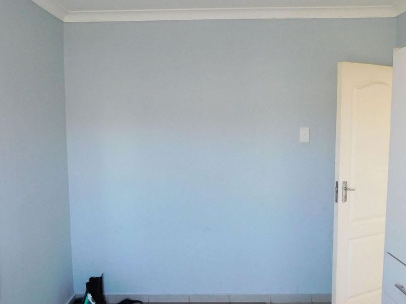 A simple bedroom featuring light blue walls, tiled flooring, and decorative coving.
