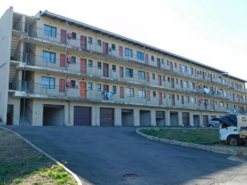 Exterior view of a multi-story apartment complex featuring ground-level garages, external balcony walkways, and an asphalt driveway.