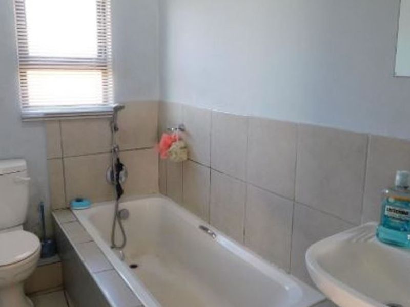 A functional bathroom featuring a bathtub with a handheld shower attachment, a pedestal basin, and a toilet, finished with neutral wall tiling.