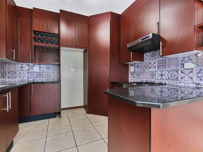 A functional kitchen featuring dark wood cabinetry, granite countertops, a decorative patterned tile backsplash, and integrated gas hob with extractor fan.