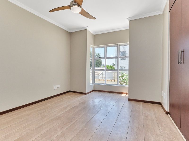 A bright and spacious bedroom featuring light laminate flooring, a ceiling fan, and a built-in cupboard, offering a clean and neutral living space.