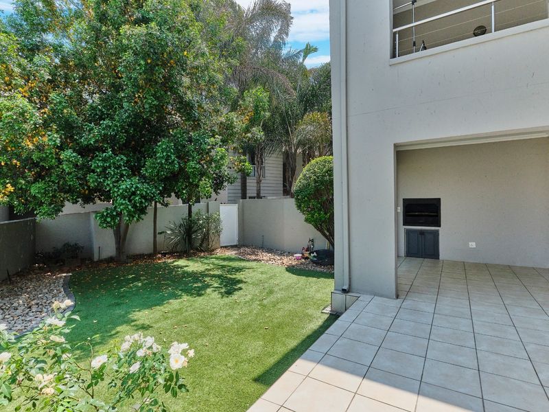 A private rear garden featuring a tiled patio with a built-in braai, artificial lawn, and established perimeter walling.