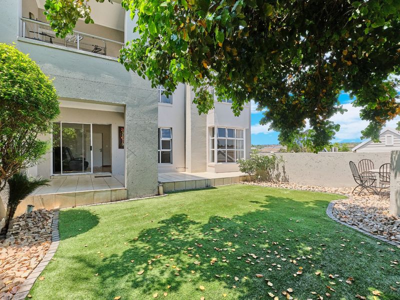A private rear garden featuring an artificial lawn, a tiled patio area, and a sliding door providing access to the apartment interior.