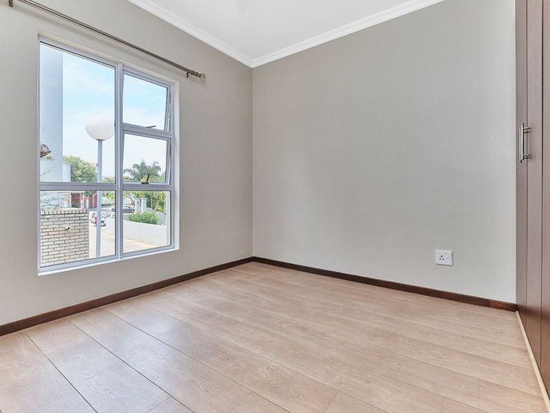 A bright, empty bedroom featuring modern laminate flooring, neutral walls, and built-in cupboards, offering a clean and versatile space.