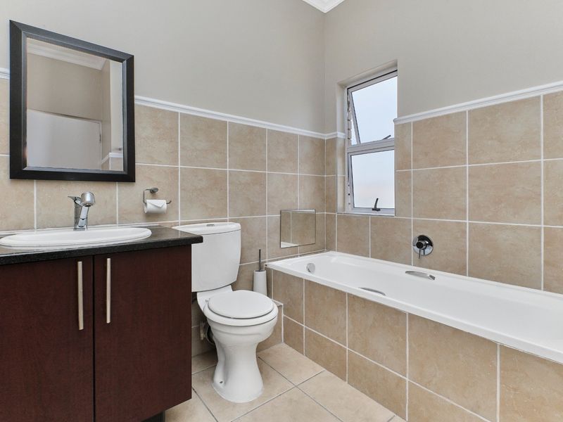 A clean and functional bathroom featuring a vanity cabinet with basin, a standard toilet, and a tiled bathtub area with neutral wall tiling.