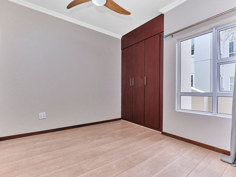 A clean, empty bedroom featuring laminate flooring, built-in dark wood cupboards, a ceiling fan, and neutral wall finishes.