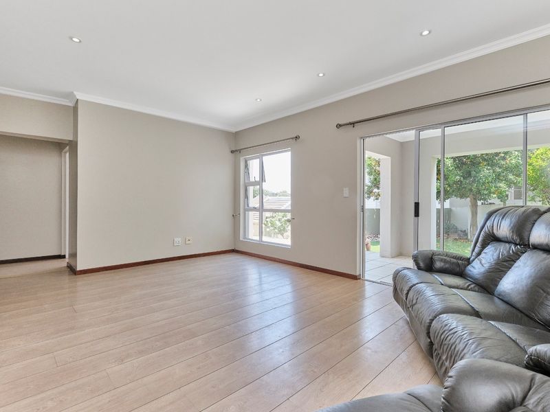 Spacious living room featuring light-toned laminate flooring, recessed downlights, and large sliding glass doors providing direct access to the outdoor patio area.