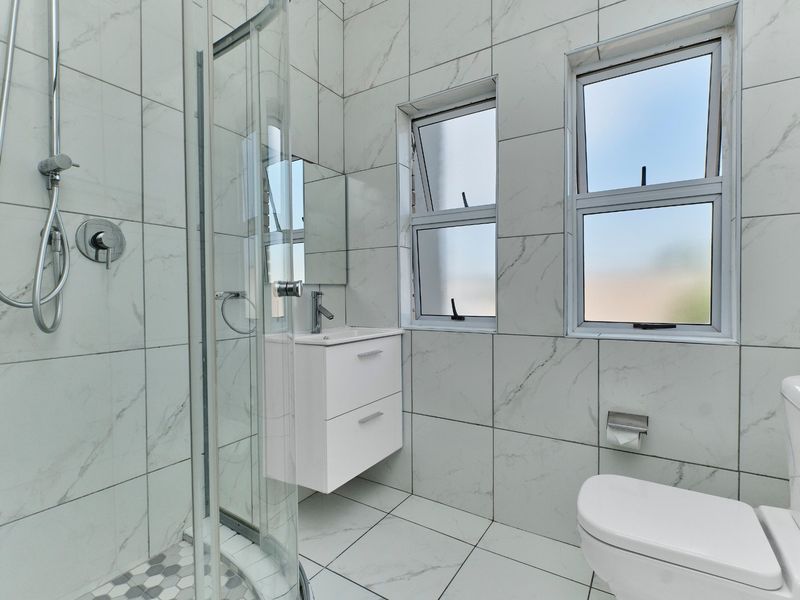 Modern bathroom featuring marble-look tiling, a glass shower enclosure, a wall-mounted vanity with basin, and a contemporary toilet.
