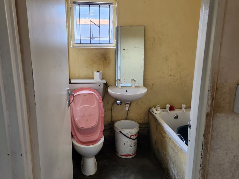 A small, dated bathroom requiring significant renovation, featuring a standard toilet, washbasin, and bathtub with visible wall surface deterioration.