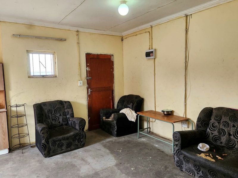 A basic living area featuring exposed electrical conduits, a security-grille window, and a timber door, requiring significant cosmetic updates and finish improvements.