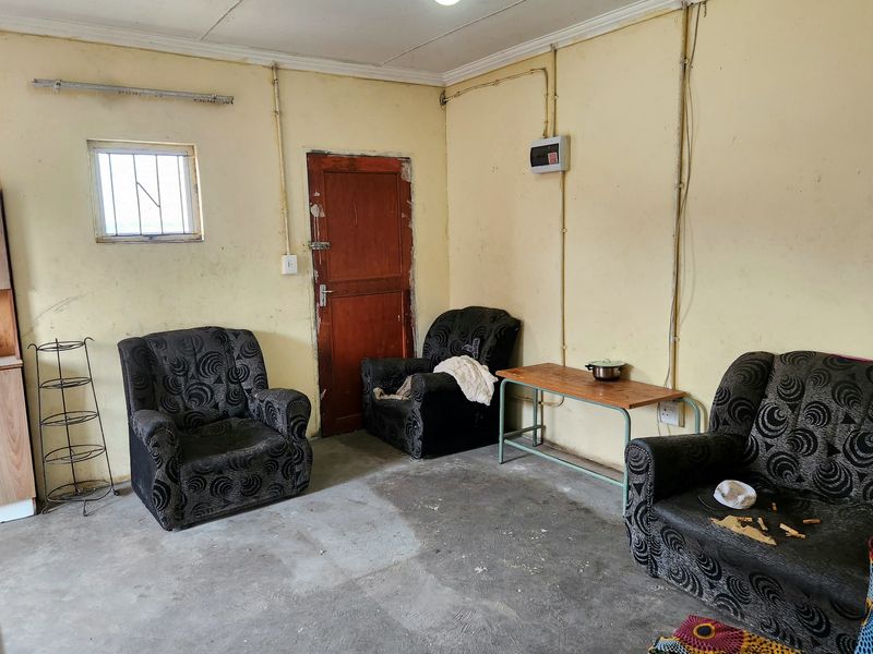 A basic living area featuring exposed electrical conduit, concrete flooring, and a timber door, requiring cosmetic updates to improve the overall finish.
