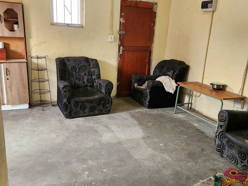 A living area featuring exposed electrical conduit, a timber door, and a concrete floor, requiring significant cosmetic updates and finish improvements.