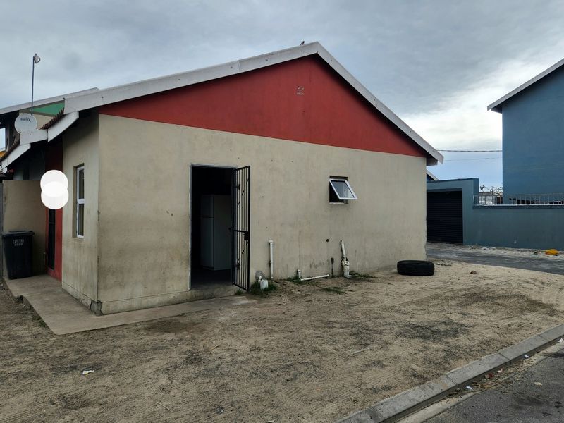 Rear view of the property showing exterior walls, security gate, and external plumbing fixtures on an unpaved yard area.