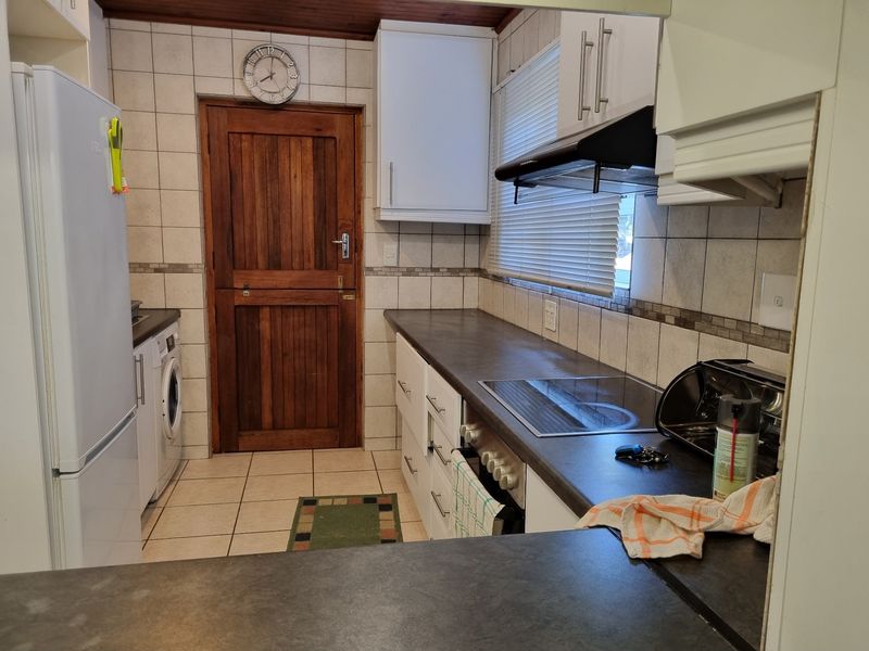 Functional kitchen featuring built-in cabinetry, dark laminate countertops, ceramic tiling, and an integrated hob with extractor fan, providing a practical workspace.