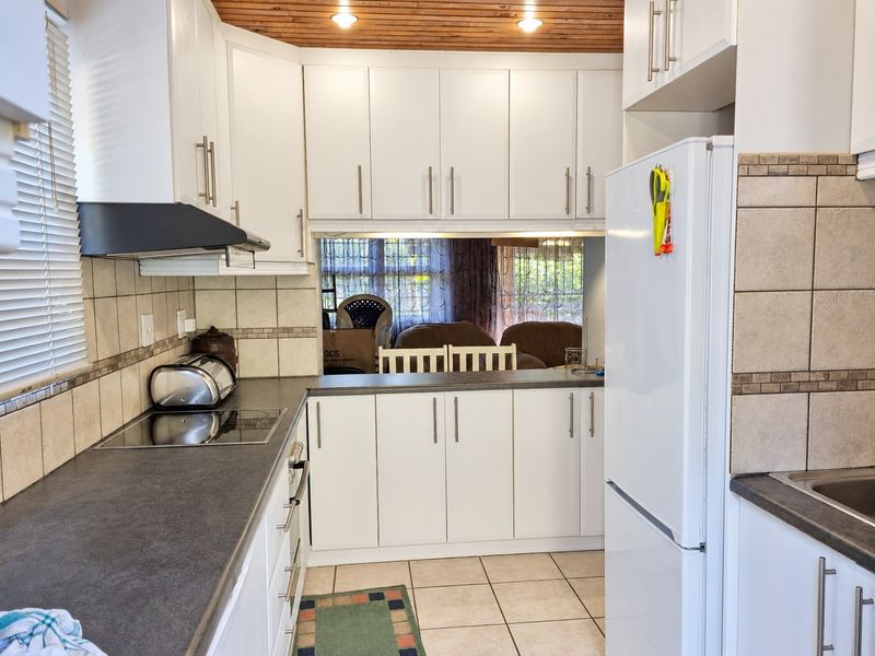 Functional kitchen featuring white cabinetry, dark laminate countertops, ceramic tile backsplash, and a warm timber ceiling with recessed lighting.