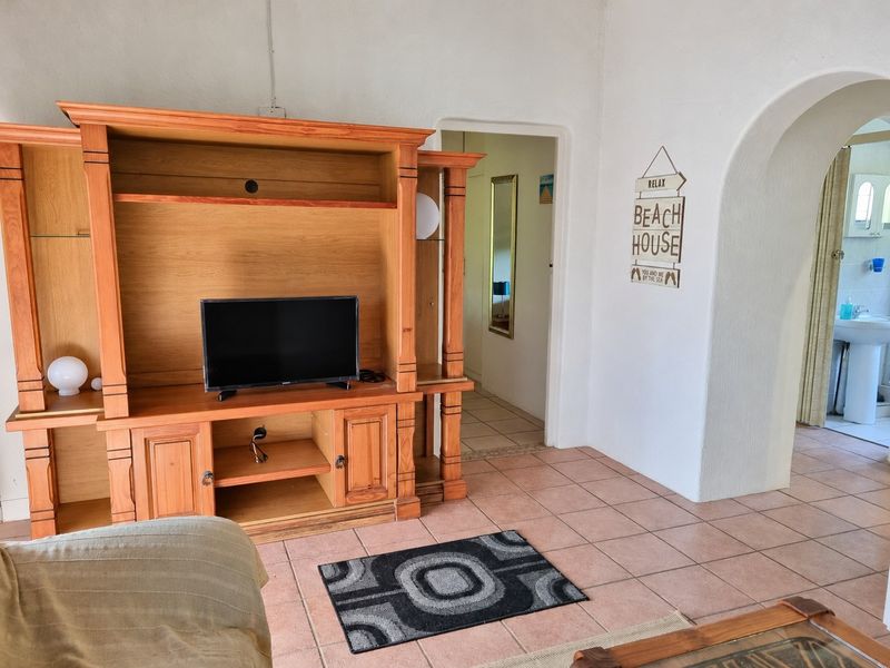 A living area featuring tiled flooring and an arched doorway leading to a hallway and bathroom.