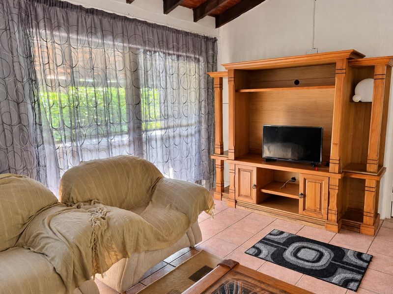 Living room featuring exposed timber ceiling beams, ceramic floor tiling, and a large sliding glass door providing natural light.