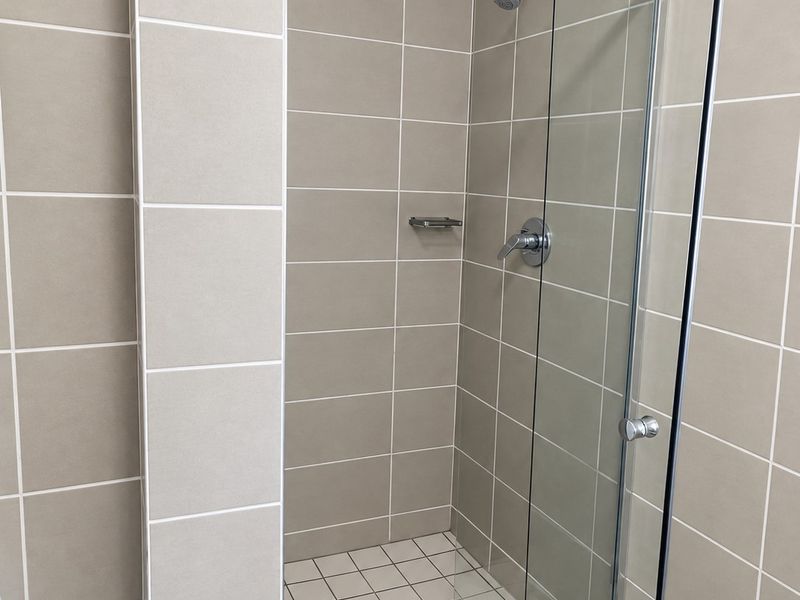 A clean and modern walk-in shower featuring neutral ceramic wall tiles, a glass enclosure, and chrome fixtures.