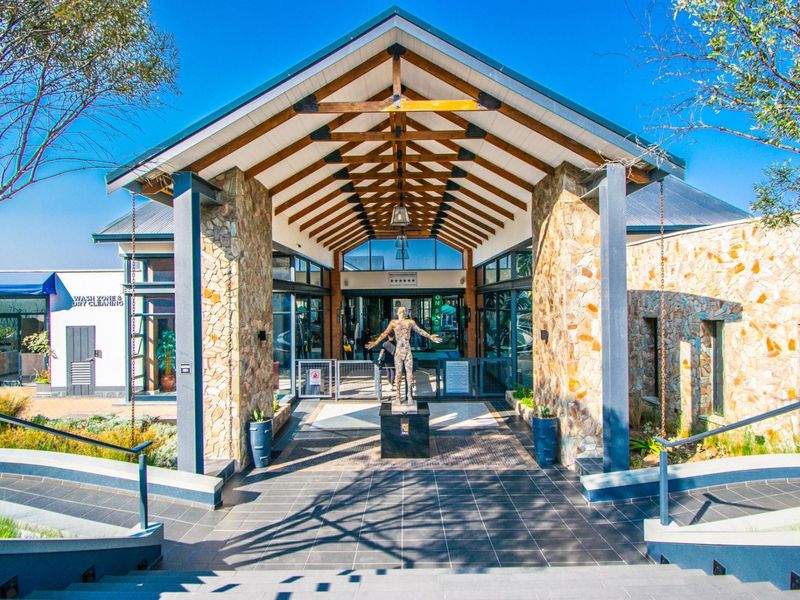 A grand entrance featuring stone-clad pillars, exposed timber roof trusses, and a tiled walkway leading into the main building complex.