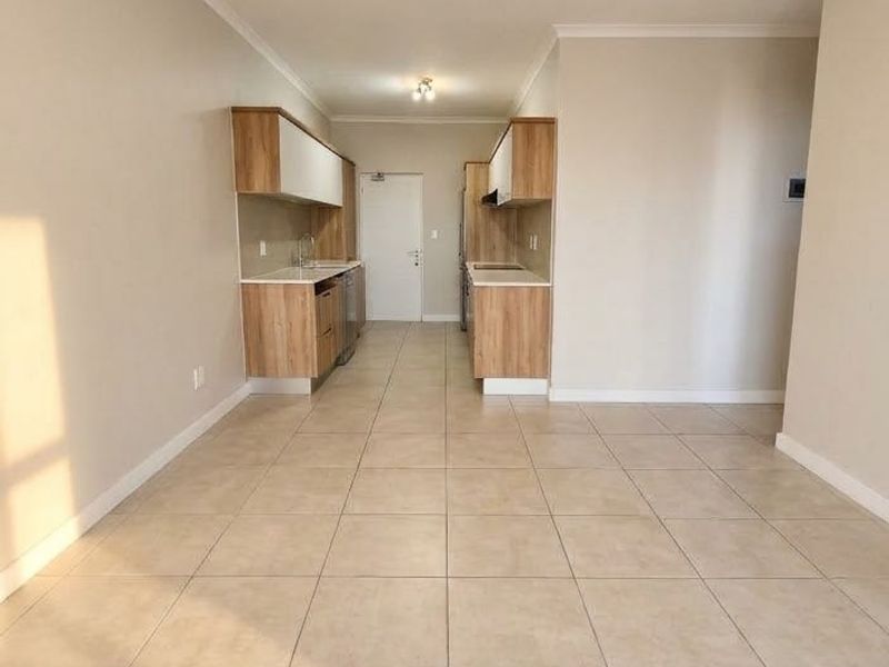 An open-plan living and kitchen area featuring neutral tiled flooring and modern wood-finish cabinetry, offering a clean and versatile space.