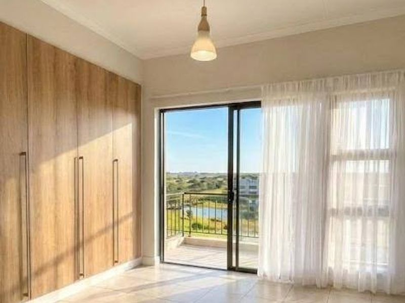 A bright, modern bedroom featuring floor-to-ceiling built-in cupboards, tiled flooring, and a sliding glass door leading to a balcony with scenic views.